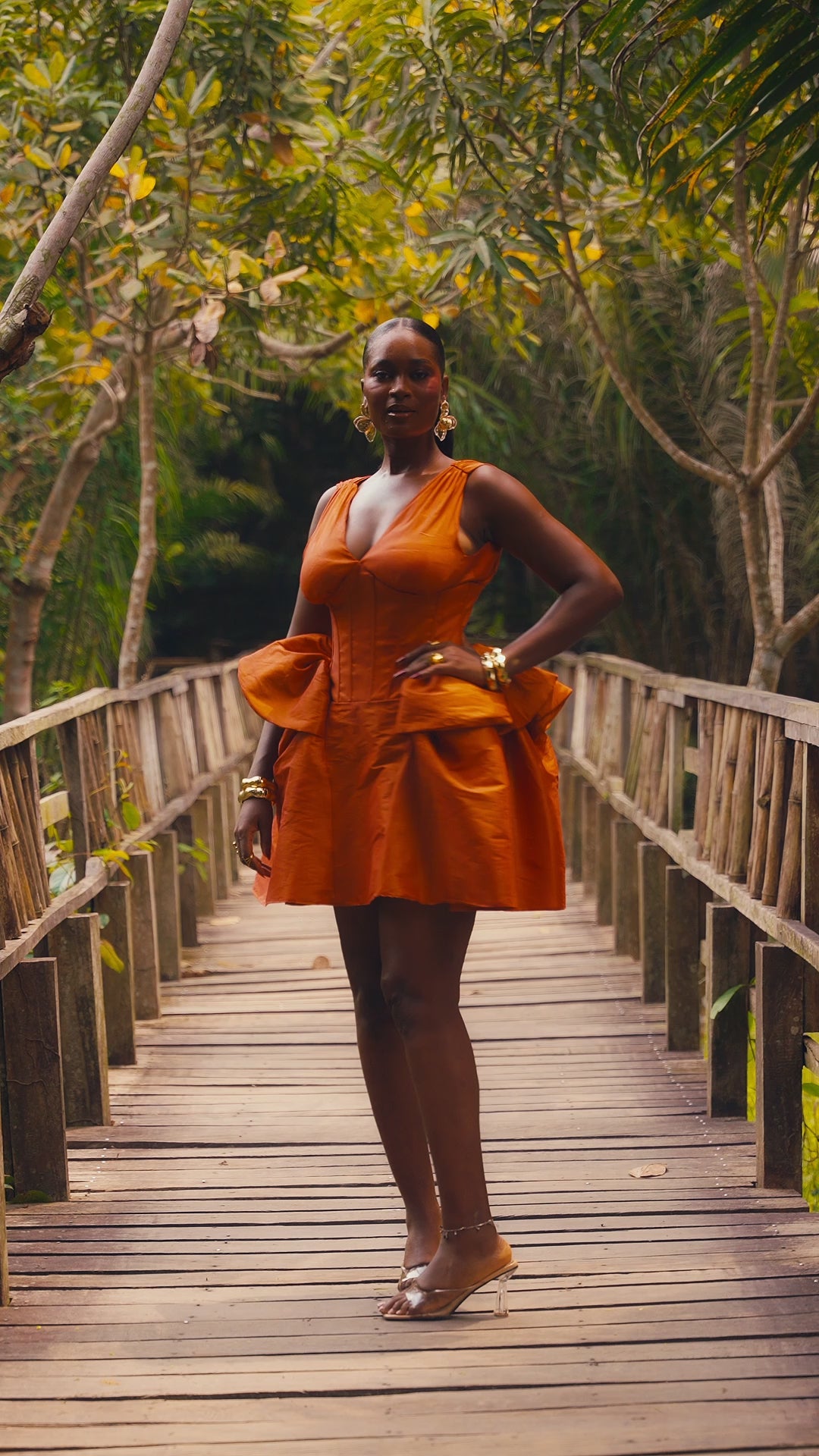Woman in burnt orange corset mini dress walking on a wooden bridge in a tropical garden
Close-up of V neckline and boned corset bodice on burnt orange dress
Side view of sculptural peplum and full skirt on orange mini dress
Back view of burnt orange mini dress showing V-back and centre zip